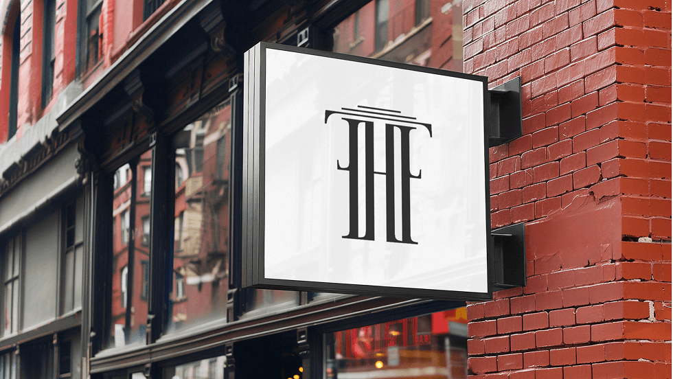 A blade sign with the monogram, mounted on a brick façade
